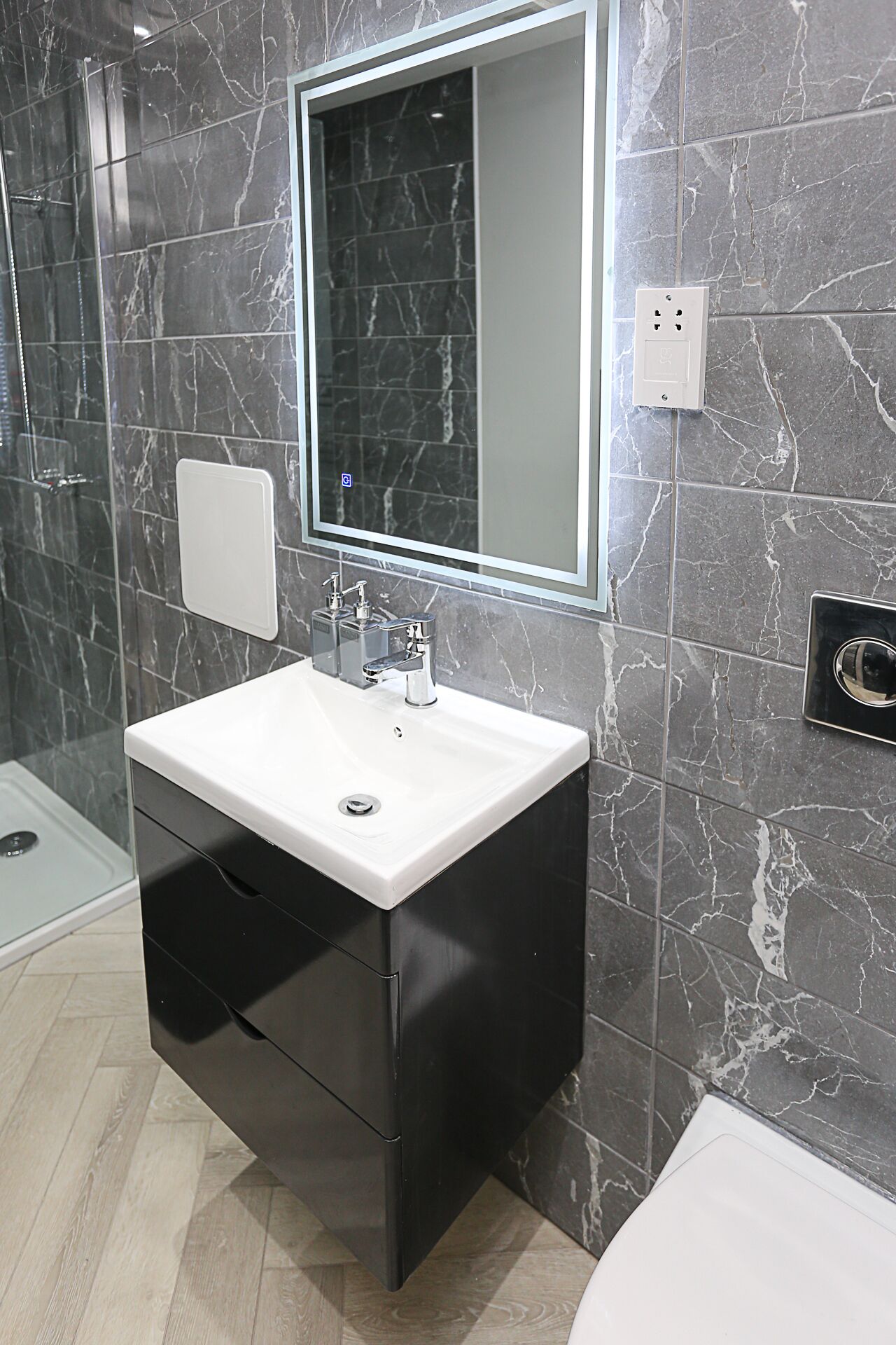 A modern bathroom with a marble-tiled wall, a white sink with a black cabinet, and a rectangular mirror.