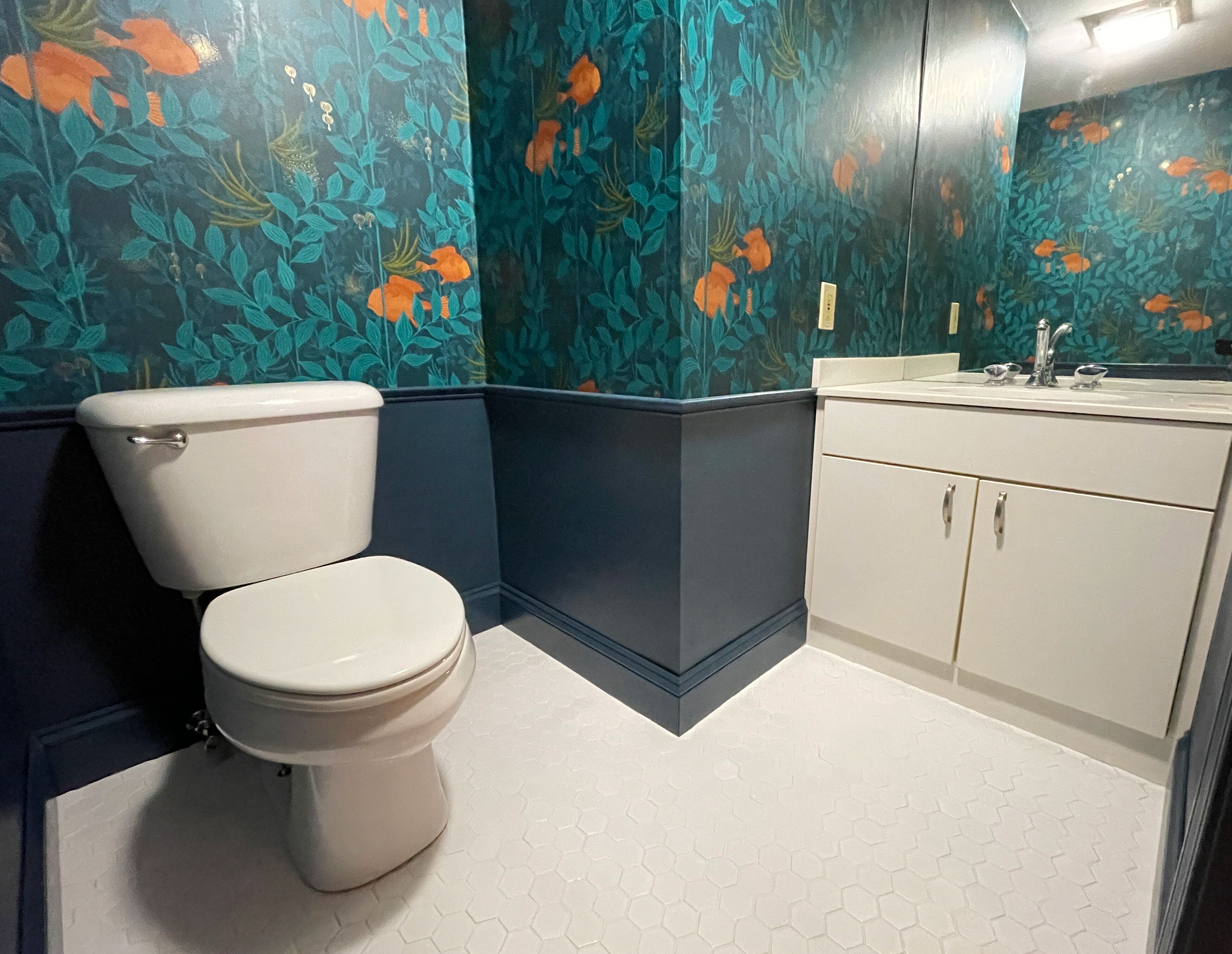 A bathroom with a toilet, a sink, and cabinets. The walls have a floral pattern.