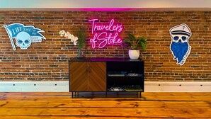 Um quarto com parede de tijolos, um letreiro de neon com a inscrição 'Travelers of Stoke', um armário de madeira e piso de madeira.
