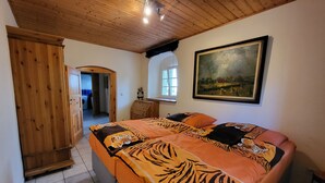 Une chambre avec un plafond en bois, un lit avec une literie à motifs de tigres, une armoire en bois et un tableau accroché au mur.