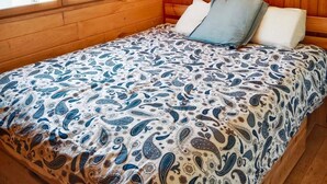 Een slaapkamer in een houten hutje met een bed, een raam en uitzicht op de natuur.