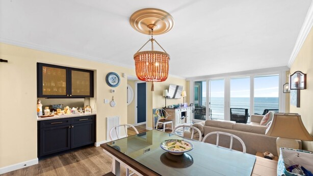 Une cuisine moderne avec une table à manger en verre, un lustre orange suspendu et une vue sur l’océan grâce à de grandes fenêtres.