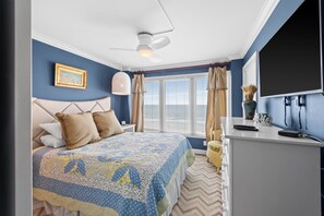 A bedroom with a bed, a desk, a TV, and a window with curtains.