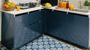 A modern kitchen with dark blue cabinets, a white tiled backsplash, a gas stove, a microwave, and a variety of fruits and beverages on the counter.