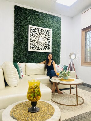 A room with a green wall, a white sofa, a round coffee table, and a decorative wall piece. - BluO Awesome 1BHK DLF Galleria Market ,Gym TT (Gurugram)