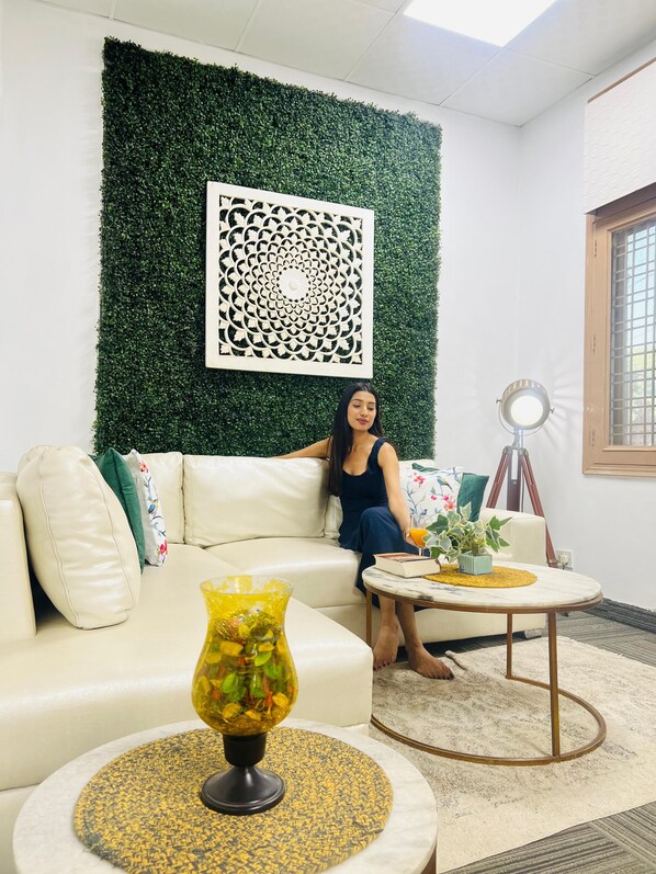 A room with a green wall, a white sofa, a round coffee table, and a decorative wall piece.