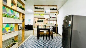 A compact kitchen with a dining table, chairs, a refrigerator, and shelves with plants.