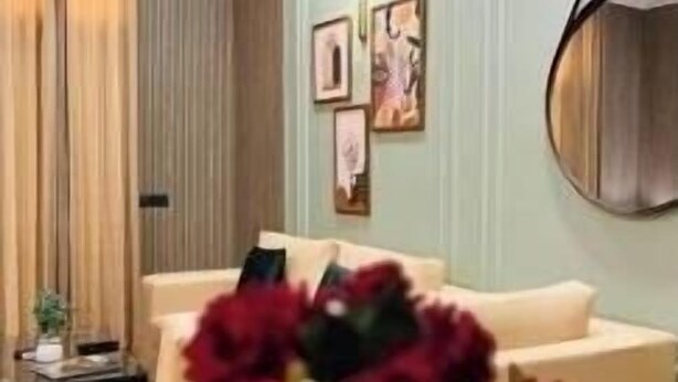 A living room with a beige sofa, a white vase with flowers, and a wall-mounted picture frame.