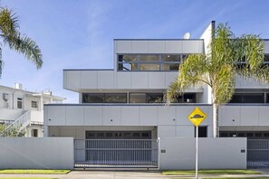 Un immeuble moderne à plusieurs étages, doté d’un toit plat, de grandes fenêtres et d’une entrée sécurisée par un portail.