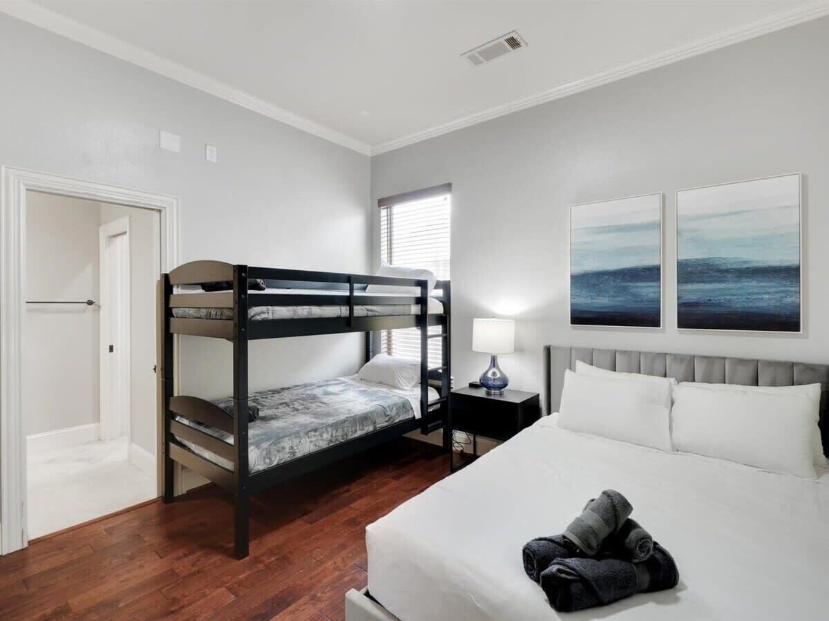 A bedroom with a bunk bed, a single bed, a nightstand with a lamp, and two wall-mounted paintings.