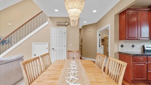 A dining area with a long wooden table, wooden chairs, a chandelier, a staircase, and a kitchen with wooden cabinets. - Close to beach, Discovery Trail, Fenced Yard (Seag) (Long Beach)