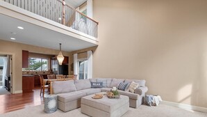 A spacious living room with a large sectional sofa, a coffee table, and a dining area with a chandelier. - Close to beach, Discovery Trail, Fenced Yard (Seag) (Long Beach)