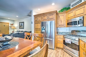 A modern kitchen with wooden cabinets, stainless steel appliances, and a dining area with a wooden table and chairs.