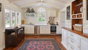 A kitchen with white cabinets, a dishwasher, an oven, and a window with a view of greenery. - Cute Cottage with Log Burning Fire, close to Wineries (Megalong Valley)