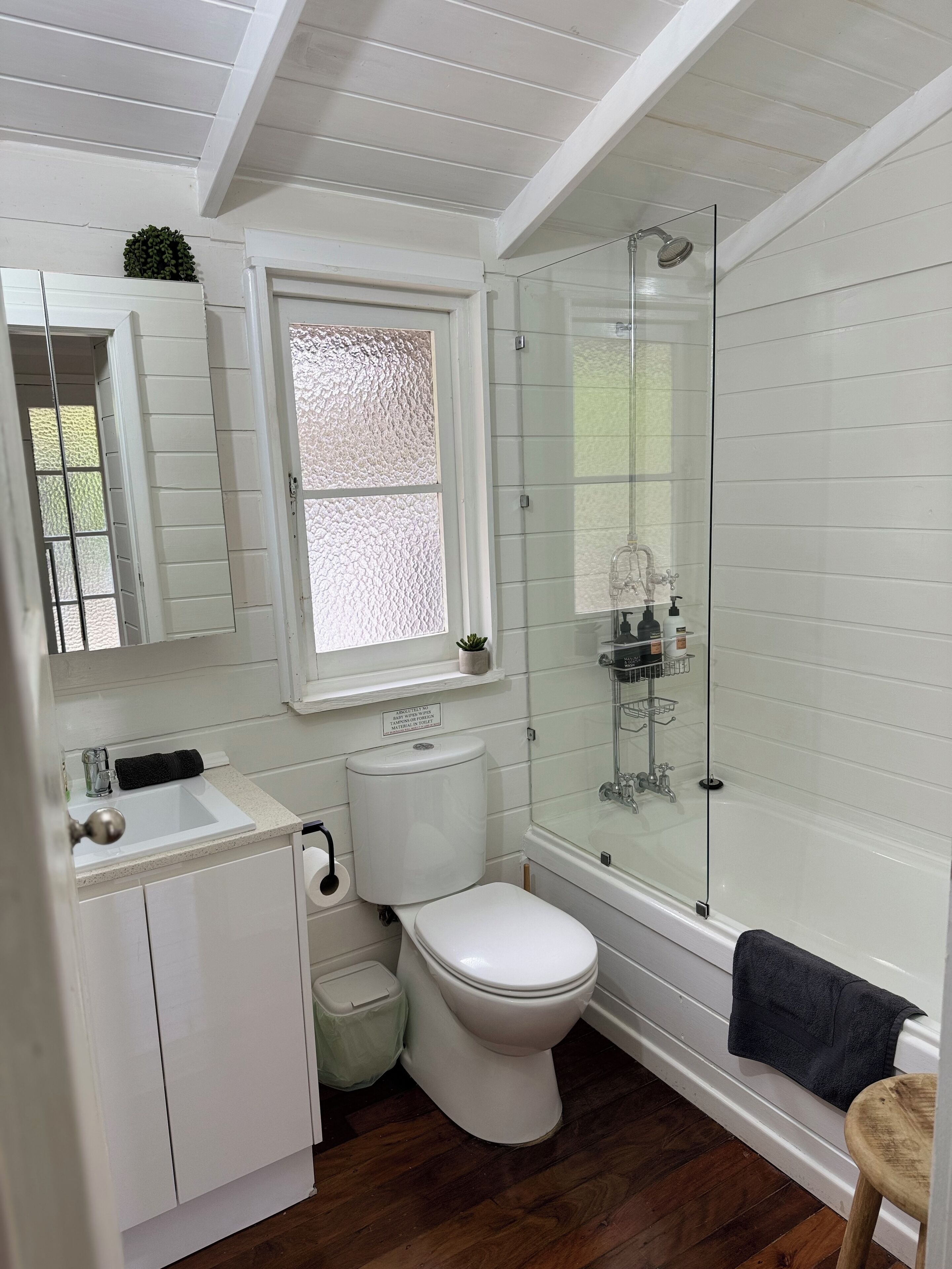 A bathroom with a white toilet, a glass-enclosed shower, a sink, and a window with frosted glass.