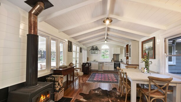 A spacious kitchen with a wood-burning stove, a dining area with a rug, and a view of the backyard through large windows. - Cute Cottage with Log Burning Fire, close to Wineries (Megalong Valley)