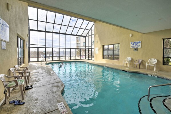 An indoor swimming pool with clear glass walls, a lifeguard sign, and several chairs along the poolside. - Ocean-View Penthouse Condo in North Myrtle Beach! (North Myrtle Beach)