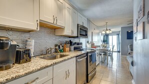 A modern kitchen with white cabinets, a granite countertop, stainless steel appliances, and a dining area with a table and chairs. - Ocean-View Penthouse Condo in North Myrtle Beach! (North Myrtle Beach)