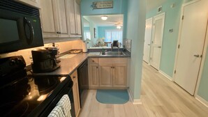 A kitchen with wooden cabinets, a black microwave, and a coffee maker. There is a blue rug on the floor and a sign on the wall.