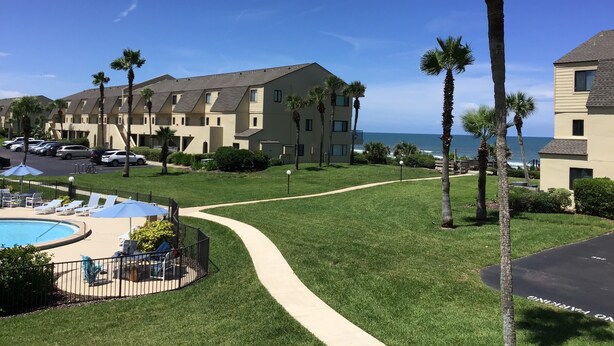 A hotel with a pool area, palm trees, and a view of the ocean.
