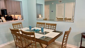 A dining area with a glass-top table, four wooden chairs, and a blue candle centerpiece.