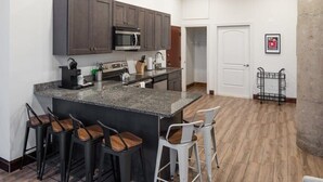 Une cuisine moderne avec des meubles de couleur sombre, un plan de travail en granit et des tabourets de bar.