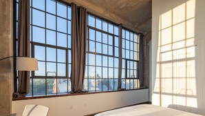 Une chambre d’hôtel avec une grande fenêtre, un lit, une chaise et une lampe.