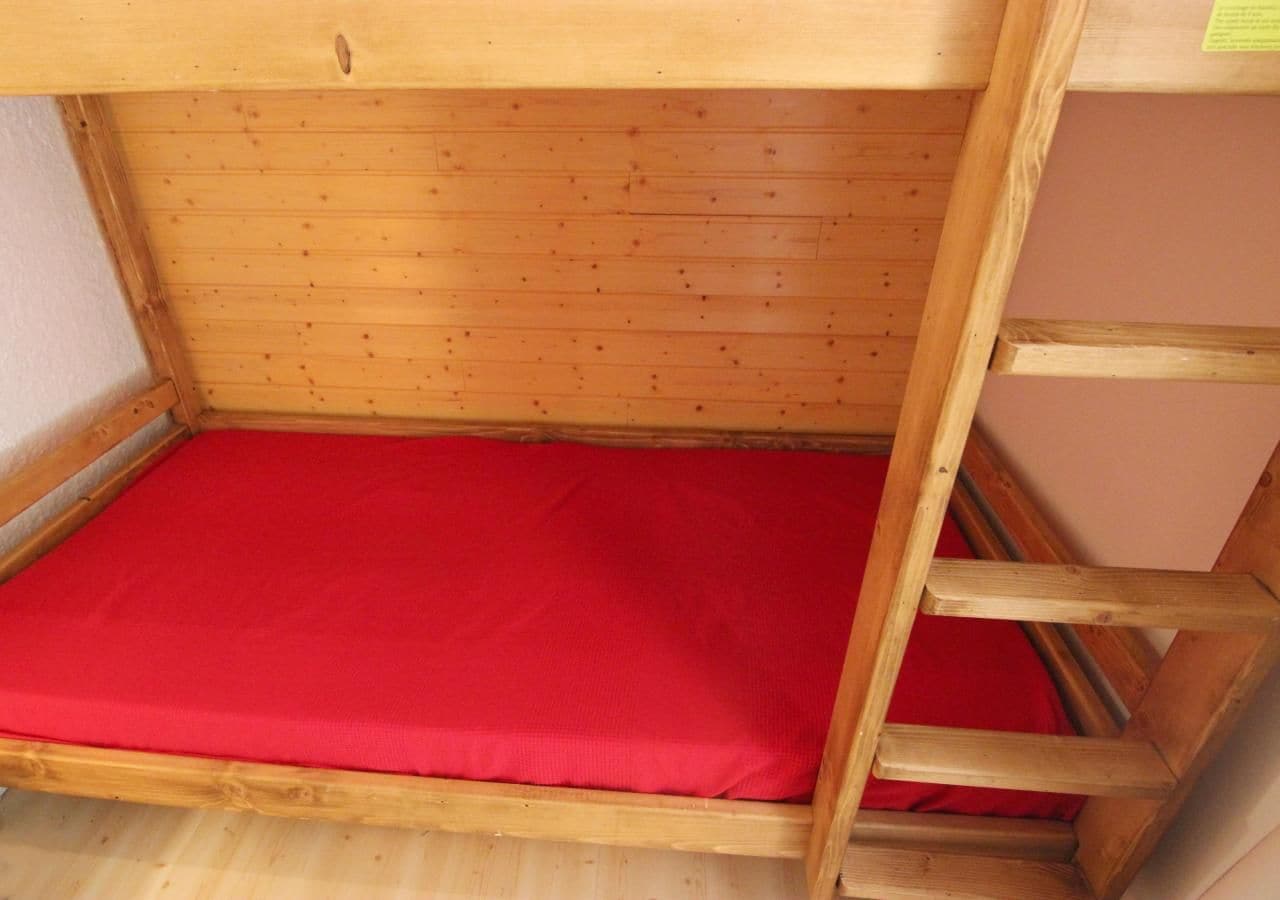A bunk bed with a red mattress and wooden frame.
