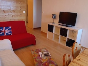 A living room with a red sofa, a white sofa, a wooden coffee table, and a TV on a white stand.