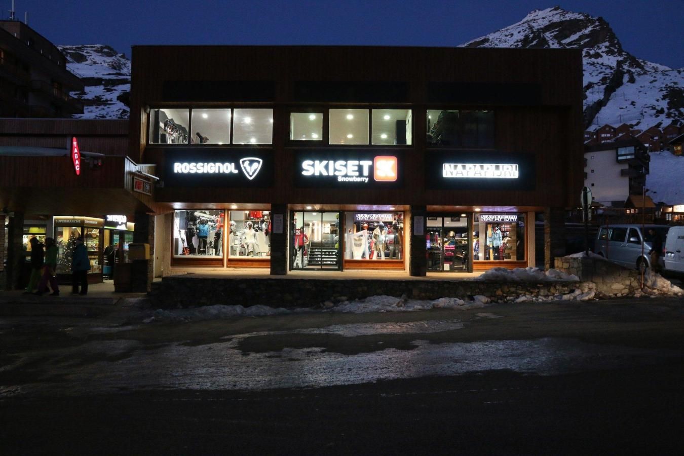 A building with storefronts for Rossignol and Skiset, featuring large glass windows and a snowy mountain backdrop.