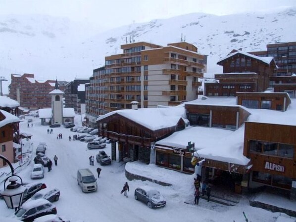 A snowy town with multi-story buildings, a central tower, and parked cars.
