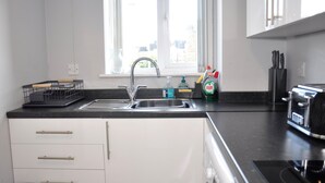 Una cucina moderna con lavello in acciaio inossidabile, mobili bianchi e piano di lavoro nero.