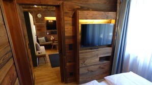 Ein Holzinterieur mit einem Bett, einem an der Wand montierten Fernseher und einer Sitzecke mit einer Couch und Sesseln.