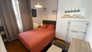 Et soveværelse med seng, et natbord, en lampe, en hængende loftlampe, et knagered og et opbevaringsskab.