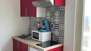 Et kompakt køkken med røde skabe, en mikrobølgeovn, elkedel og backsplash-fliser med mønster.