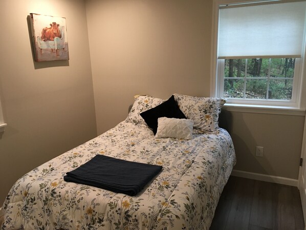 A bedroom with a floral bedspread, a black folded blanket, and a window with a view of trees. - Fully remodeled house with amazing views. (Fairfield)