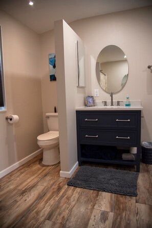 A bathroom with a toilet, a dark vanity with drawers, a round mirror, and a small framed picture on the wall. - Fully remodeled house with amazing views. (Fairfield)