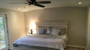 Ein Schlafzimmer mit einem Bett, einem Deckenventilator, einem Nachttisch mit Lampe und Blick durch eine Glastür.