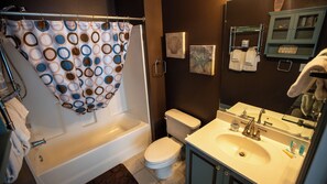 Ein Badezimmer mit Badewanne, Toilette, Waschbecken und einer Duschvorhang mit einem kreisförmigen Muster.