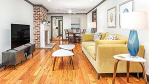 A modern living room with a brick accent wall, a sofa, a coffee table, and a TV. - Waldburg Garden by Tybee Vacation Rentals (Savannah)