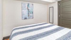 A bedroom with a bed, a painting on the wall, and a door. - Waldburg Garden by Tybee Vacation Rentals (Savannah)