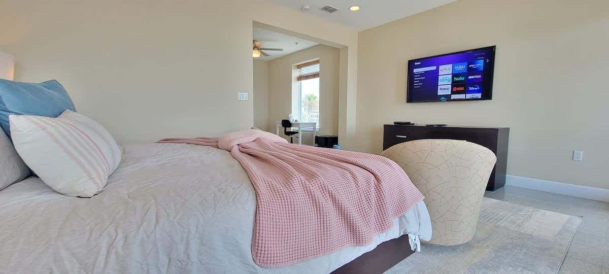 A bedroom with a large bed, a desk, and a television on the wall.