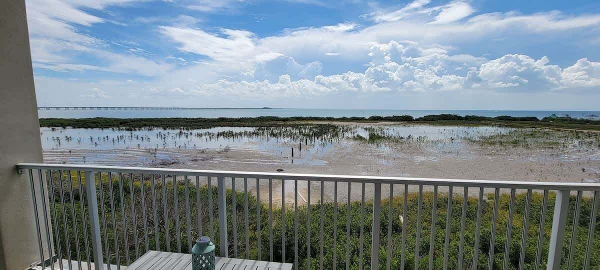 Een balkon met uitzicht op een kustgebied, inclusief een strand en een wateroppervlak.