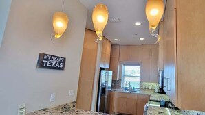 A modern kitchen with wooden cabinets, a built-in oven, and a window providing natural light. - Tortuga Bay 3 Bedroom Home by RedAwning (South Padre Island)