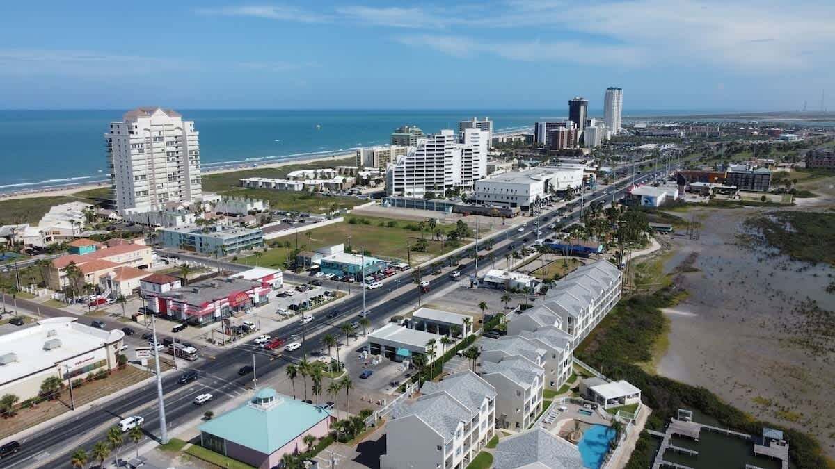 An aerial view of a coastal city with a prominent hotel, a highway, and a beach.