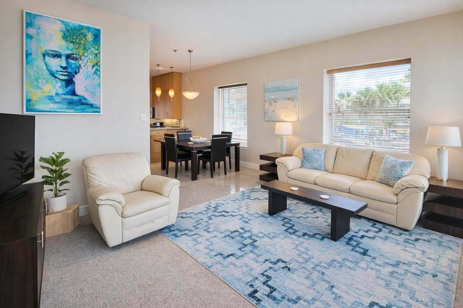 A modern living room with a sofa, armchair, coffee table, and a dining area with a table and chairs.
