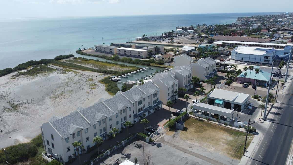 An aerial view of a coastal hotel with multiple buildings, a beach in the foreground, and a clear view of the ocean.