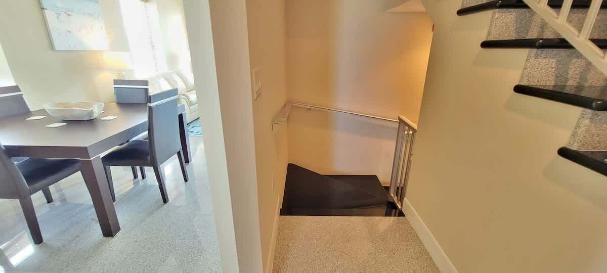 A staircase with a handrail, carpeted steps, and a dining area with a table and chairs in the background.