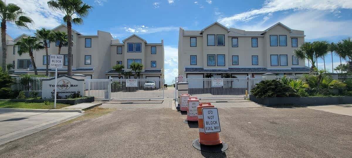 Un área residencial cerrada con varias casas de dos pisos, cielo despejado y un letrero que indica 'TOFUGA BAY'.