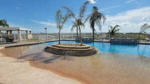 A swimming pool with a circular island, palm trees, and a fenced area with chairs. - Tortuga Bay 3 Bedroom Home by RedAwning (South Padre Island)